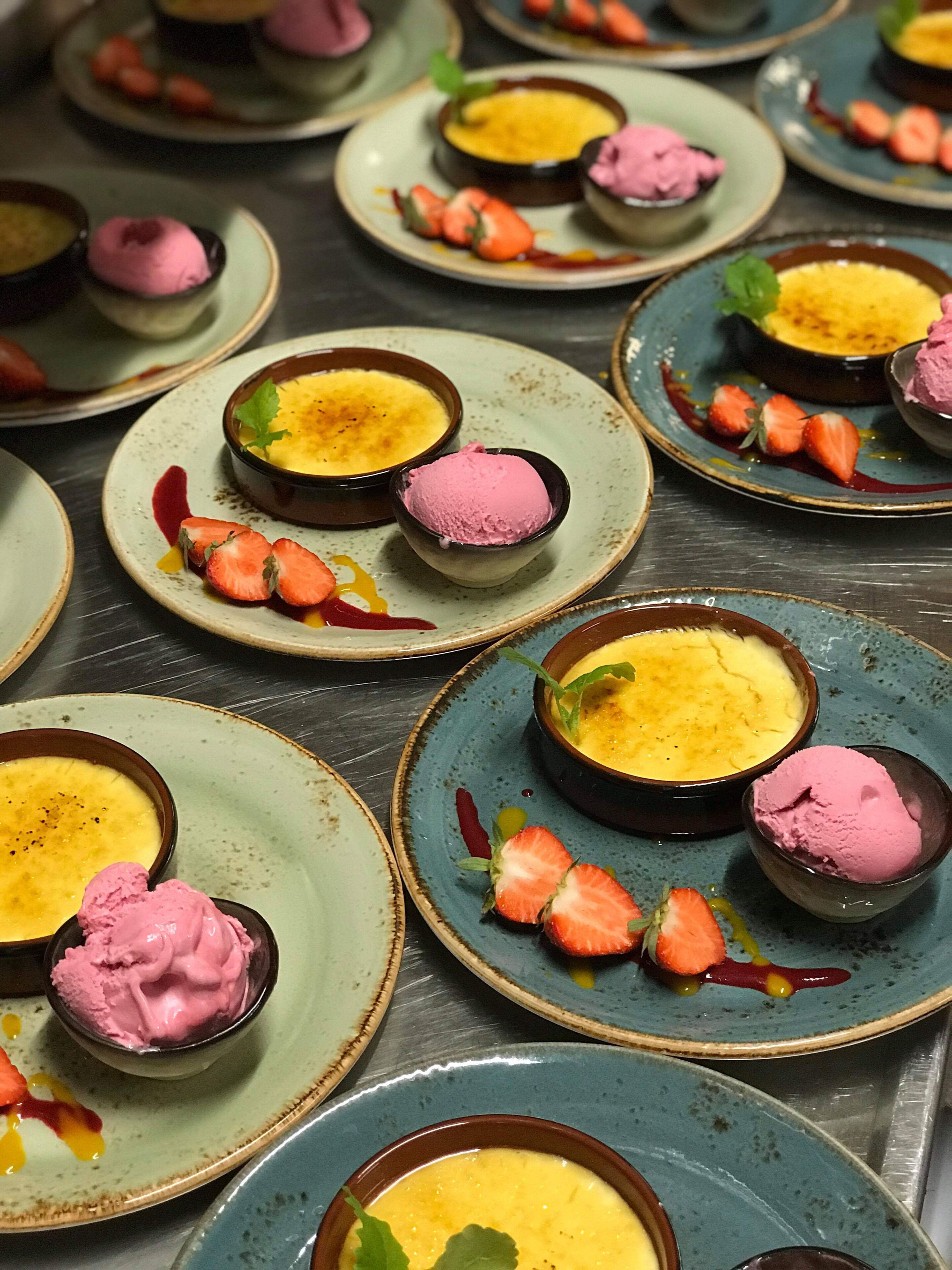 Une présentation de desserts comprenant plusieurs assiettes de crème anglaise et de glace rose, décorées de fraises et de feuilles de menthe.