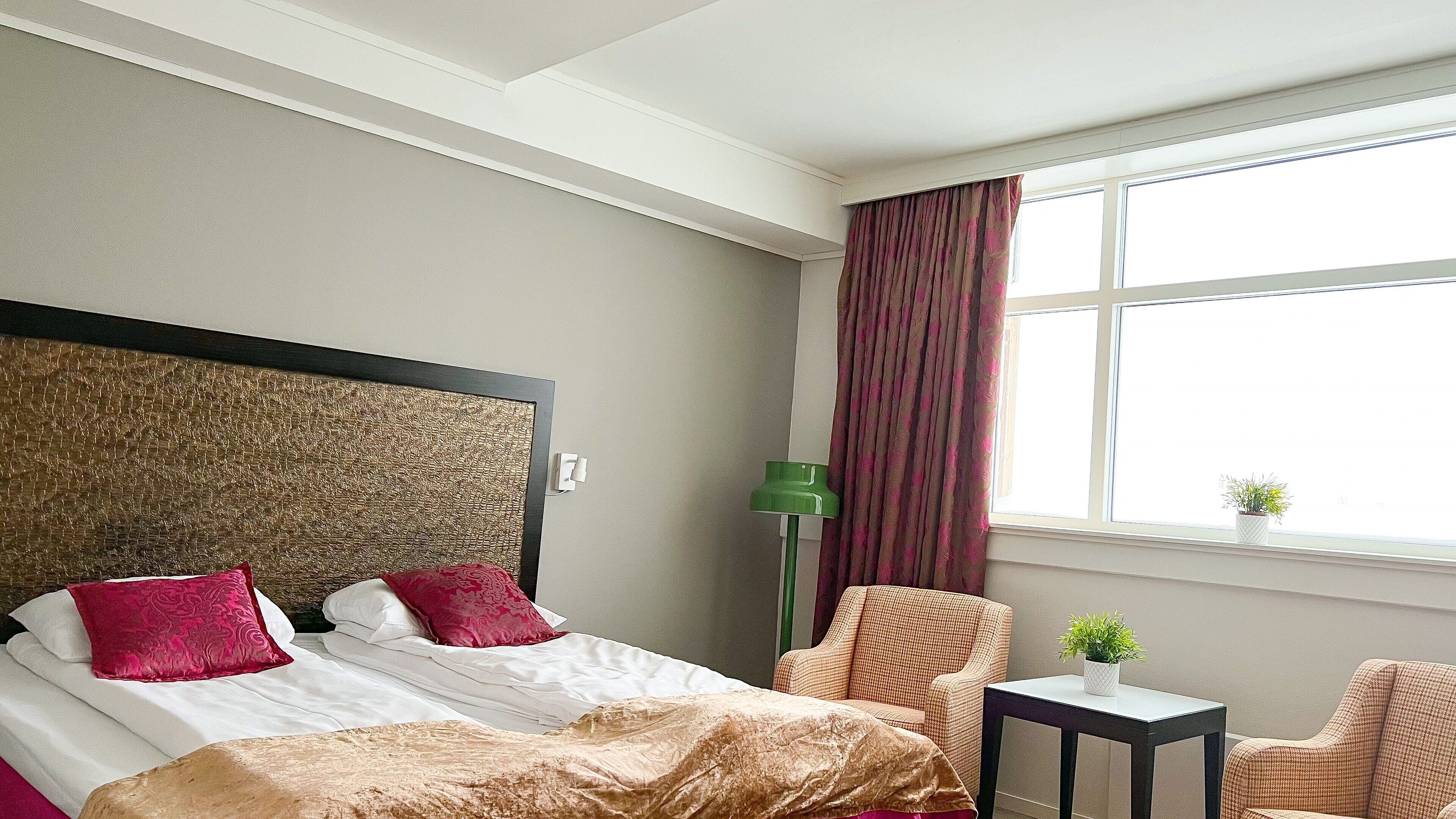 Una habitación de hotel con cama, una silla, una mesita y una ventana con cortinas.