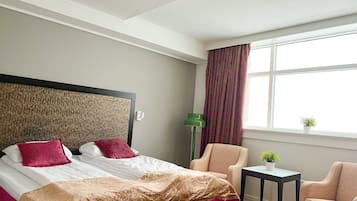 Una habitación de hotel con cama, una silla, una mesita y una ventana con cortinas.