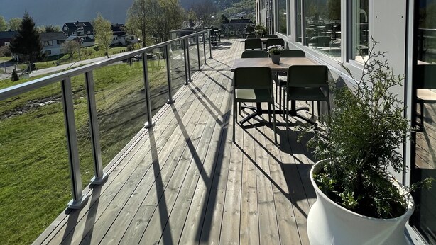 Una terraza de madera con mobiliario exterior, una planta en maceta y vistas a montañas al fondo.