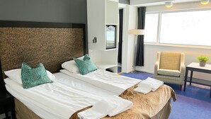 Habitación de hotel con dos camas, una silla, una mesita con una planta y una ventana con cortinas.