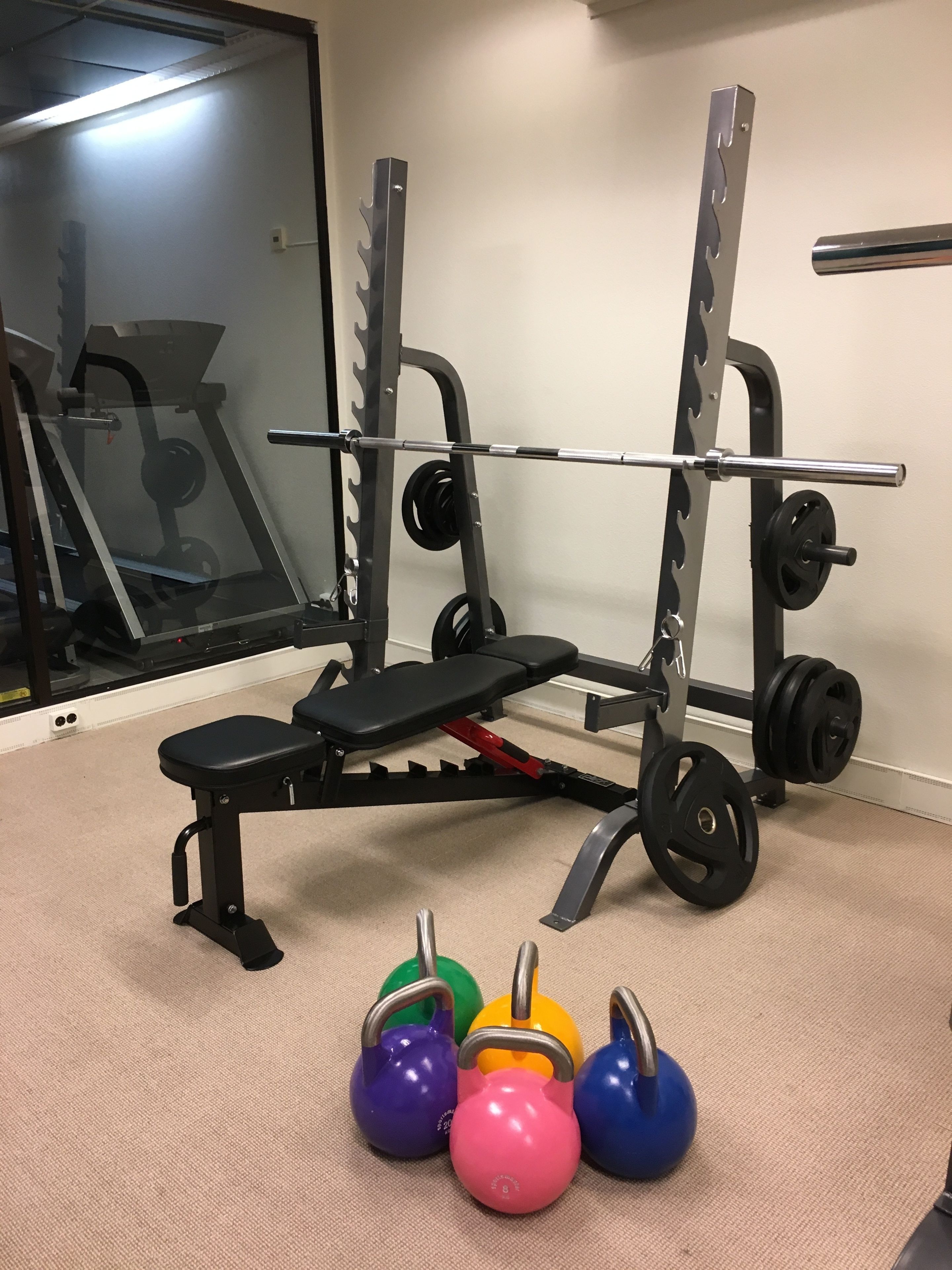 A gym with a bench, squat rack, and kettlebells.