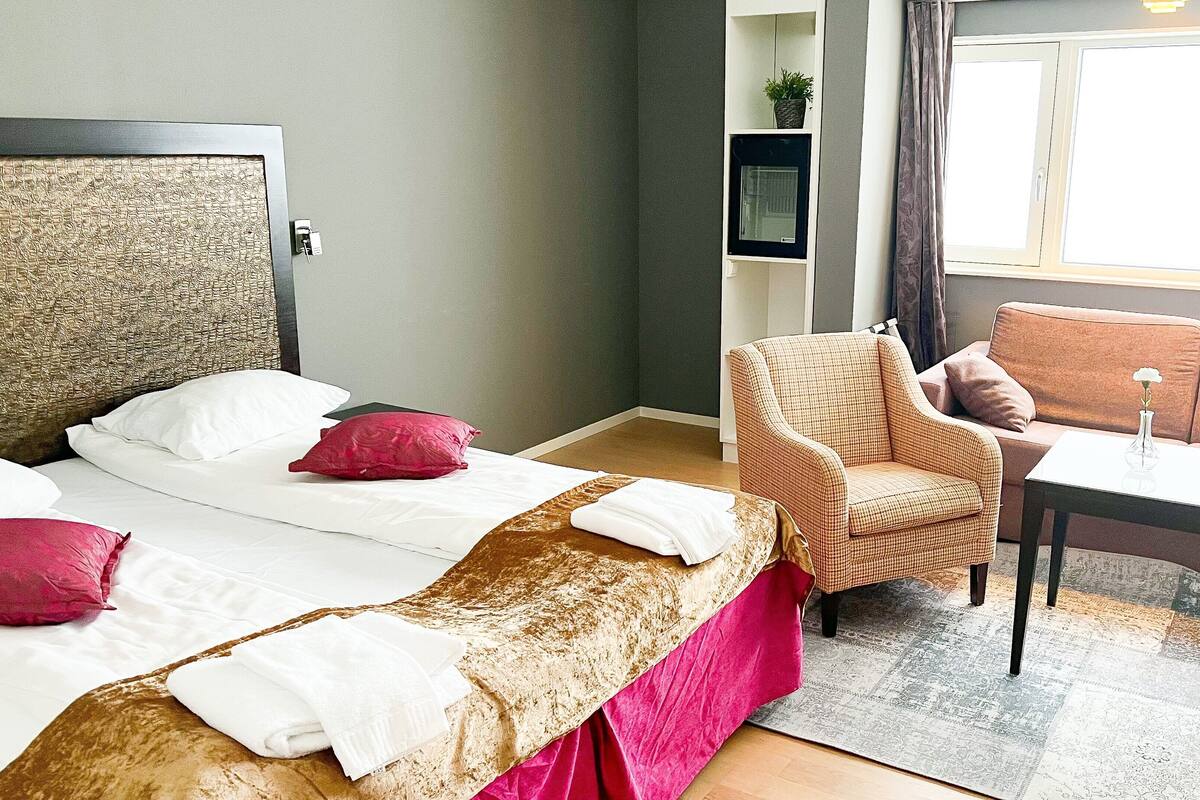 A hotel room with a bed, two chairs, a small table, and a sofa.