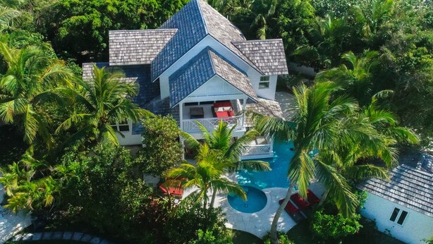 An aerial view of a house with a unique triangular roof, surrounded by lush greenery and a swimming pool. - BREATHTAKING : on water front with panoramic views + pool + dock (Harbour Island)