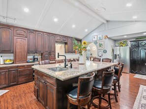 A spacious kitchen with a large island, dark wooden cabinets, and a stainless steel refrigerator.