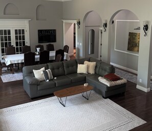 A living room with a sectional sofa, a coffee table, and a dining area with a table and chairs. - Luxurious Private Estate with Hot Tub. Game Room, Grand Piano- Near Ski Resort (Salt Lake City)