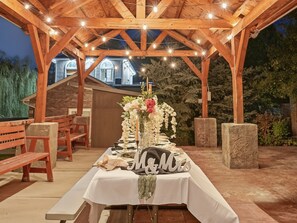 Un área de comedor al aire libre con una pérgola de madera, luces colgantes y una mesa lista para una comida.