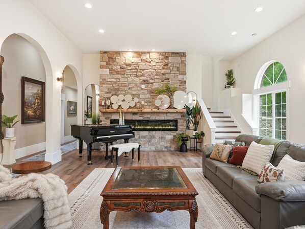 A spacious living room with a stone fireplace, a grand piano, and a comfortable seating area.