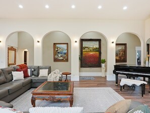 A spacious living room with a grand piano, a sectional sofa, and three framed paintings on the wall.