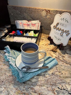 Eine Kaffeetasse auf einer Marmorplatte, zusammen mit einem Löffel, einer Taschentuchbox und einem Schild mit der Aufschrift 'Kindness changes everything'.
