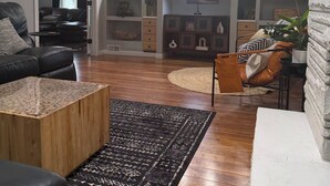 Un salón con un sofá de cuero negro, una mesa de centro de madera, un tapete estampado y una pared de acento de piedra.