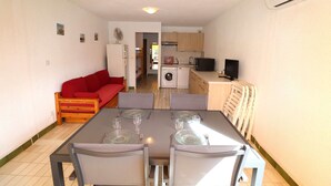 Un espace de vie compact comprenant une table à manger pour quatre personnes, un canapé rouge, un lave-linge, un petit coin cuisine et un téléviseur.