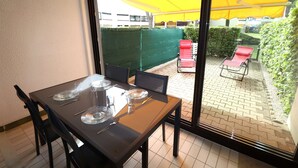 Un coin repas avec une table dressée pour quatre personnes, une porte-fenêtre coulissante donnant sur une terrasse extérieure agrémentée d’un parasol jaune et de chaises rouges.