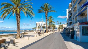 Un paseo marítimo con palmeras, bancos y un edificio que anuncia pizza y pasta.