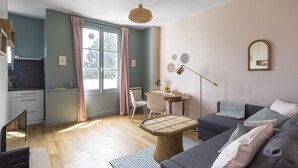 Ein modernes Wohnzimmer mit einer Couch, einem Esstisch und einer Küchenzeile mit Fenster und Vorhängen.