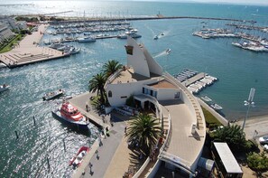 A marina with boats docked, a pedestrian walkway, and a building with a unique architectural design.