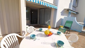 An outdoor dining area with a white table, blue and white striped awning, and white plastic chairs.