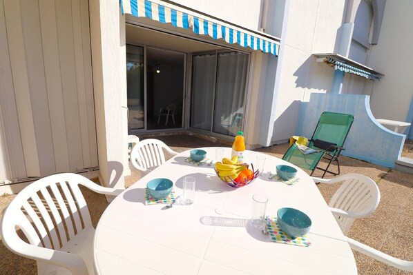 An outdoor dining area with a white table, blue and white striped awning, and white plastic chairs.