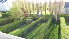 Ein gepflegter Garten mit ordentlich geschnittenen Hecken und Bäumen, einem deutlich sichtbaren Weg und einem Gebäude im Hintergrund.