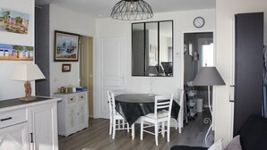 A dining area with a round table, white chairs, a black tablecloth, and a pendant light. There is a white cabinet with drawers and a painting on the wall.