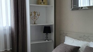 A bedroom with a bed, a white wardrobe, a mirror, and a hanging light fixture.