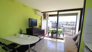 Ein gemütliches Zimmer mit Bett, Esstisch und Stühlen, Fernseher und Balkon mit Blick auf Gebäude.