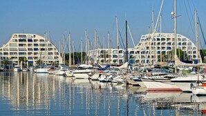 Ein Yachthafen mit mehreren angemeldeten Booten, ein großes Gebäude mit Balkonen und ein klarer, blauer Himmel.