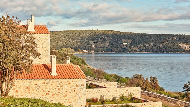 A stone building with a tiled roof overlooking a lake, surrounded by greenery and hills. - 100 Rizes Seaside Resort - Small Luxury Hotels of The World (East Mani)