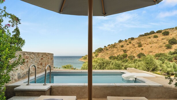 A poolside area with two lounge chairs, a stone wall, and a view of the sea. - 100 Rizes Seaside Resort - Small Luxury Hotels of The World (East Mani)