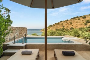 A poolside area with two lounge chairs, a stone wall, and a view of the sea. - 100 Rizes Seaside Resort - Small Luxury Hotels of The World (East Mani)