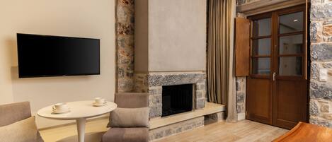 A modern living room with a stone fireplace, a flat-screen TV mounted on the wall, a round table with two chairs, and a wooden bench.