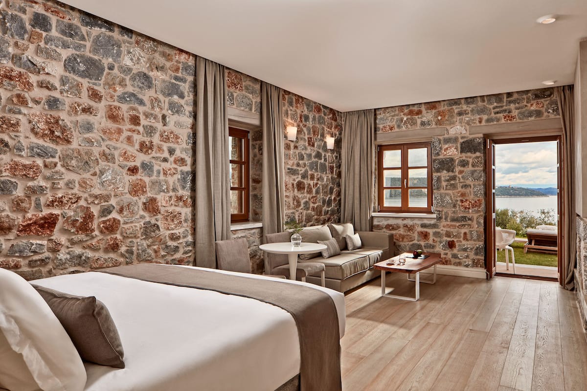 A room with a stone wall, a bed, a sofa, a small table, and a view of the outdoors.