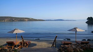 A beach with lounge chairs and umbrellas, a rocky shoreline, and a calm sea. - 100 Rizes Seaside Resort - Small Luxury Hotels of The World (East Mani)