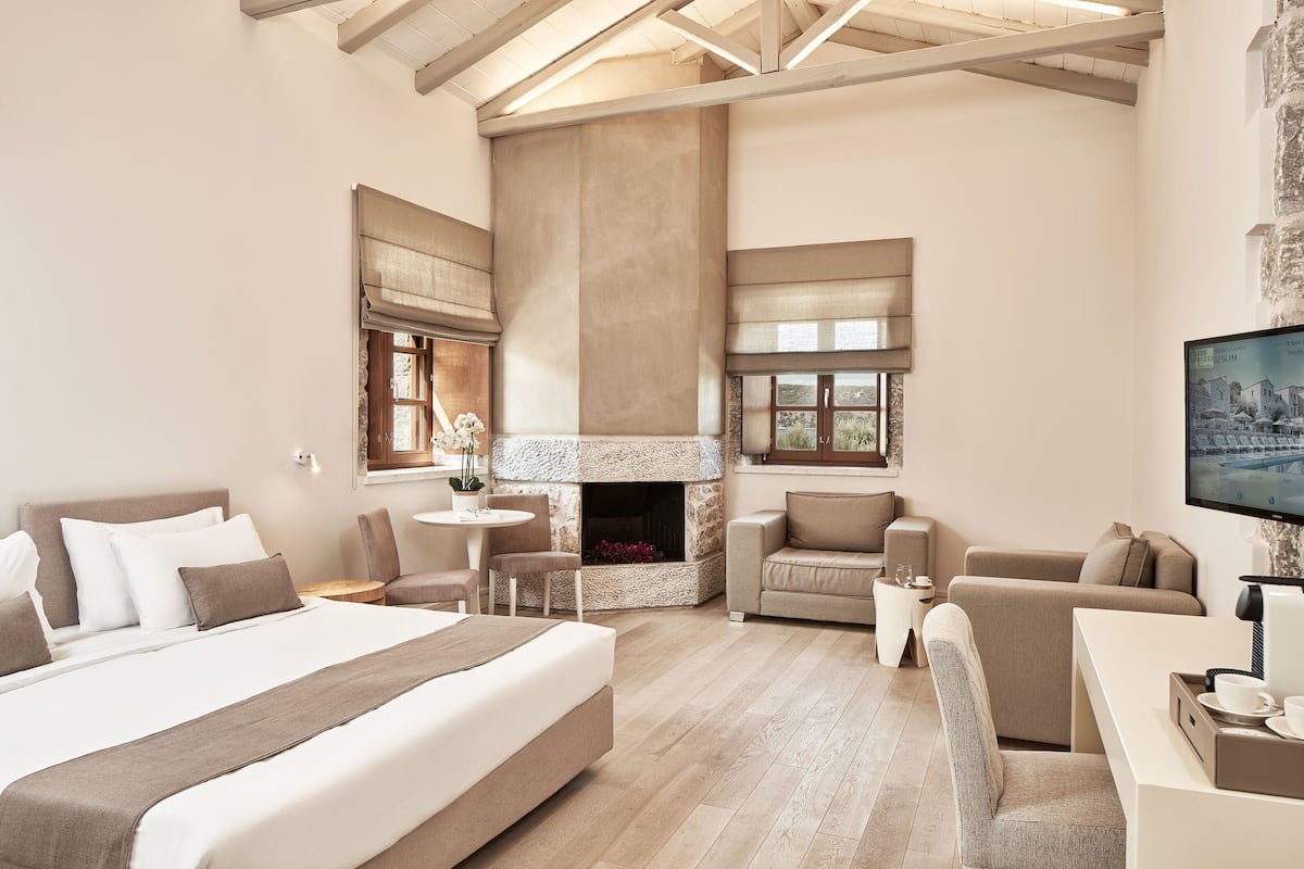 A spacious bedroom with a large bed, a fireplace, a seating area with a sofa and chairs, and a television on the wall.