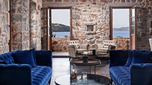 A room with stone walls, a view of the sea, two blue sofas, and a fireplace. - 100 Rizes Seaside Resort - Small Luxury Hotels of The World (East Mani)