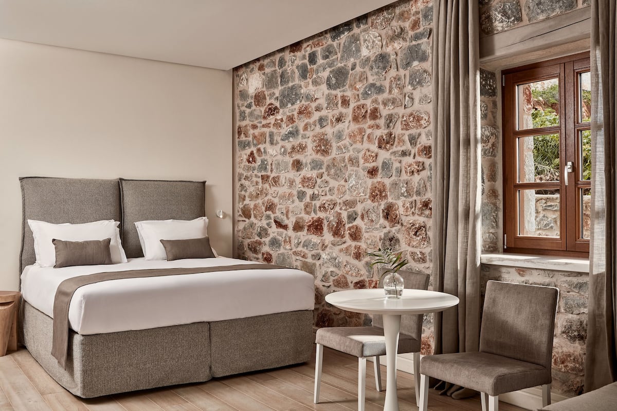 A bedroom with a stone wall, a bed, a round table, and a chair.