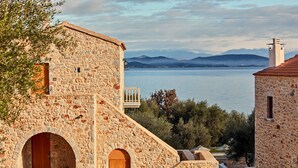A stone building with a wooden door and an arched window, overlooking a body of water and mountains. - 100 Rizes Seaside Resort - Small Luxury Hotels of The World (East Mani)