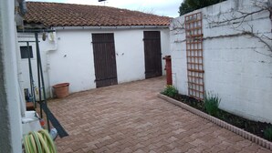 A paved courtyard with a tiled roof, a white wall with a wooden gate, and a small garden area. - HOUSE RENTAL 12 PEOPLE OLERON  (Saint-Pierre-d'Oléron)
