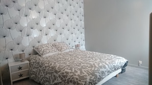 A bedroom with a patterned bedspread, a nightstand with a lamp, and a wall with a leaf pattern. - HOUSE RENTAL 12 PEOPLE OLERON  (Saint-Pierre-d'Oléron)