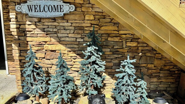 A stone wall with a 'WELCOME' sign, decorative evergreen trees, and a bear statue holding a sign.