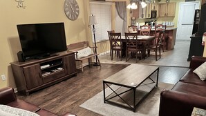 A living room with a TV, leather sofa, coffee table, and dining area with chairs and a table.