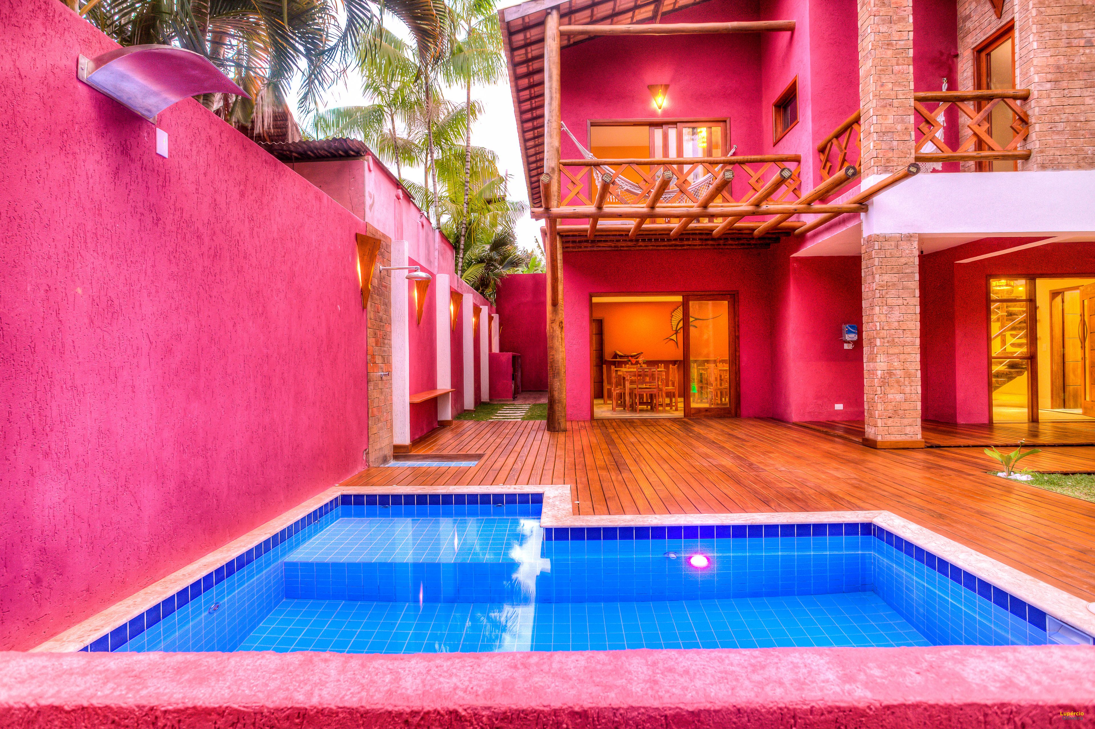 A pool area with a wooden deck and a red building with a balcony.