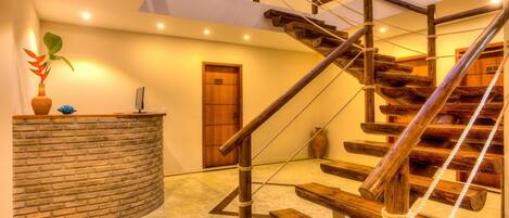 Una escalera de madera con barandilla de cuerda, un mostrador de recepción de piedra y una puerta de madera en un interior moderno.