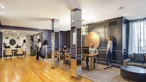 A modern hotel lobby with a reception desk, seating area, and a large mirror reflecting the space. - The Sire Hotel Lexington,tapestry Collection by Hi (Lexington)