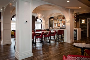 A spacious bar area with a long counter, red chairs, and a chandelier.
