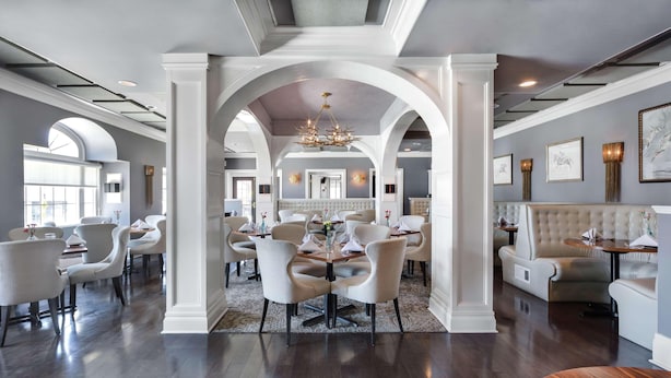 A spacious dining area with high ceilings, arched doorways, and a chandelier. Tables are set with white tablecloths and chairs. - The Sire Hotel Lexington,tapestry Collection by Hi (Lexington)