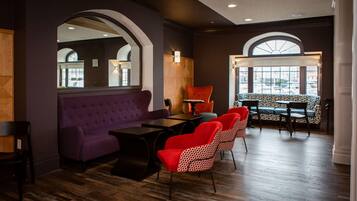 A modern interior with a purple sofa, red chairs, a wooden table, and a patterned bench.