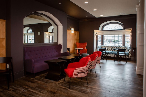 A modern interior with a purple sofa, red chairs, a wooden table, and a patterned bench.