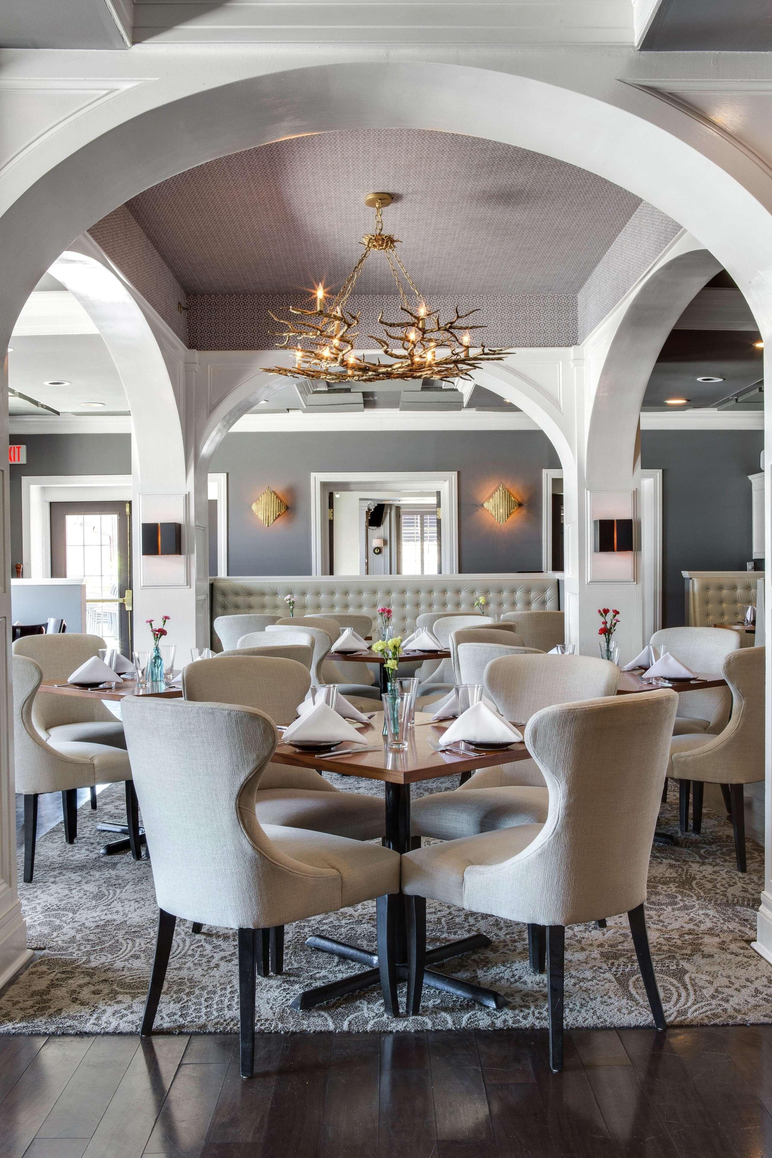 A dining area with a round table, upholstered chairs, a chandelier, and a tufted bench in the background.