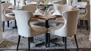 A dining area with a round table, upholstered chairs, a chandelier, and a tufted bench in the background. - The Sire Hotel Lexington,tapestry Collection by Hi (Lexington)